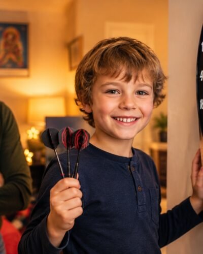 Young child smiling holding soft tip darts at a kids dartboard with parent nearby
